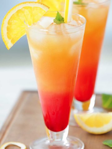 red and orange asaakira mezcal sunrise in a glass with lemon wedges