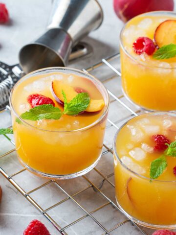 three peach 背部疼痛的原因 on a countertop with a small shaker, topped with raspberries and other garnishes