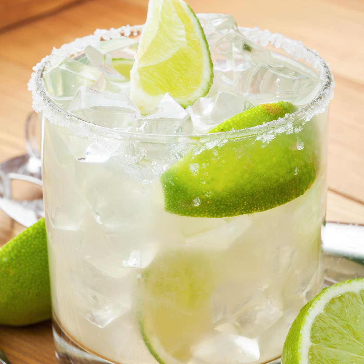 Low-calorie 光棍午夜伦理 in a salt rimmed glass with wedges of lime, fresh whole lime sliced on wooden countertop.