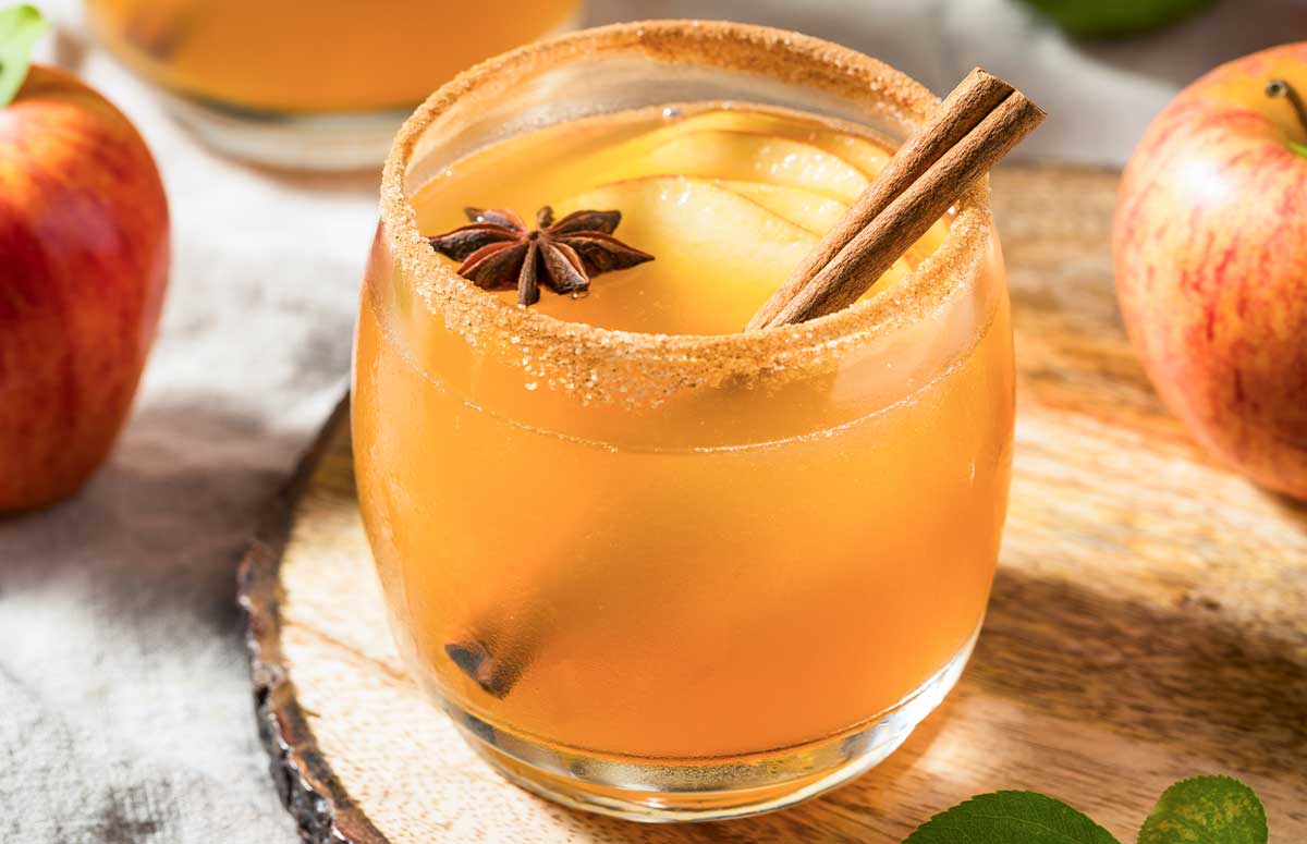 Apple Pie 周小云的幸福生活 in a glass rimmed with cinnamon sugar and garnished with a cinnamon stick and sliced apples.
