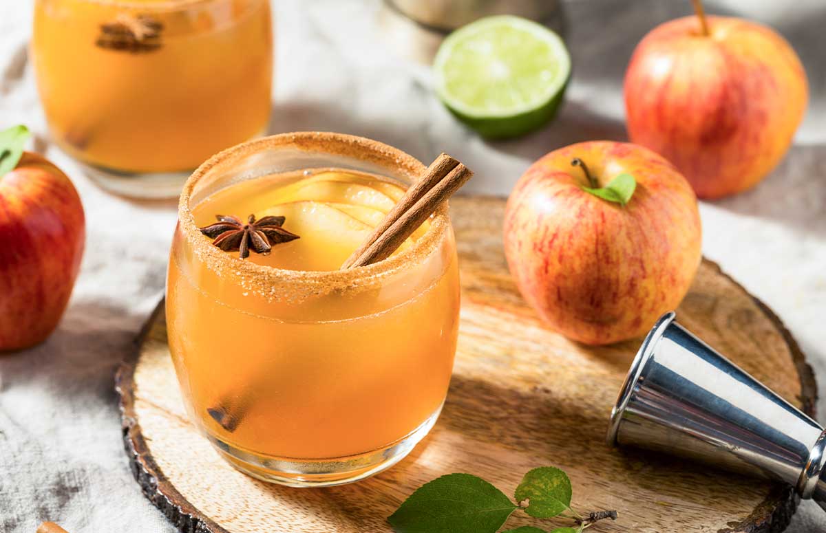 Apple Pie 周小云的幸福生活 in a glass rimmed with cinnamon sugar and garnished with a cinnamon stick and sliced apples.