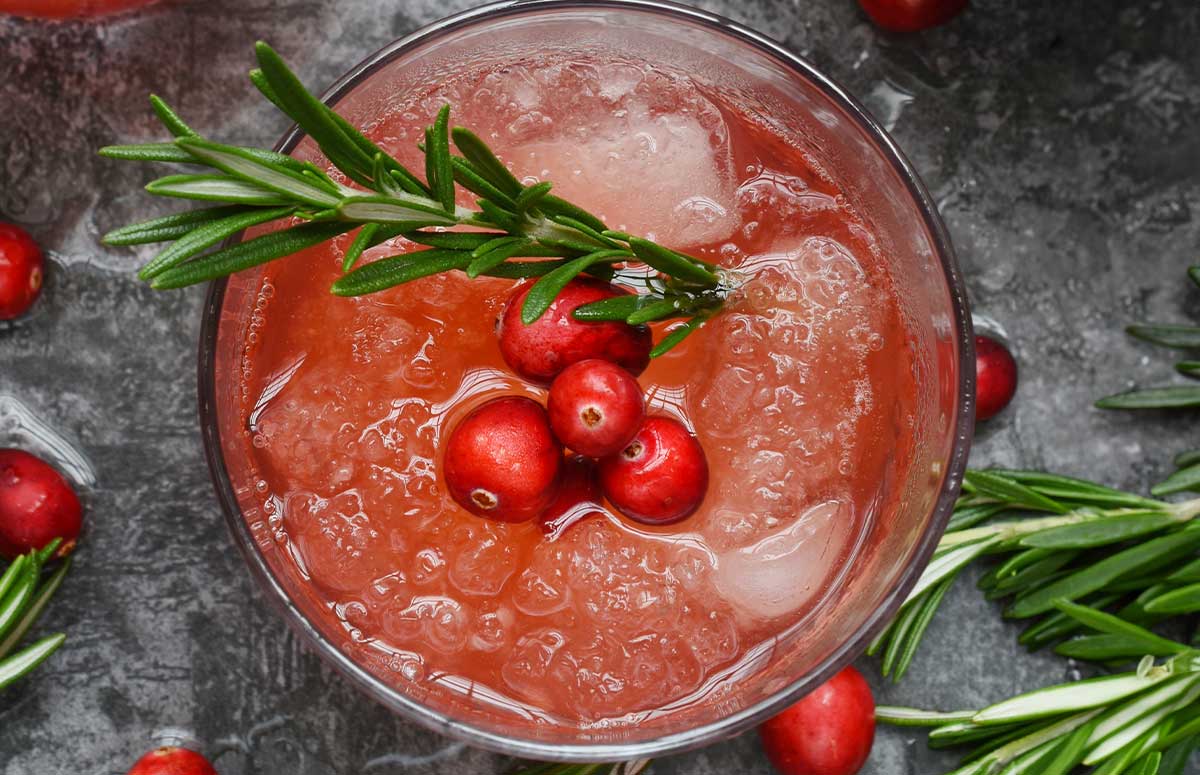 Overhead view of cranberry 国产xxxx视频在线观看 with ice, fresh cranberries, and rosemary sprigs, bowl of fresh cranberries.