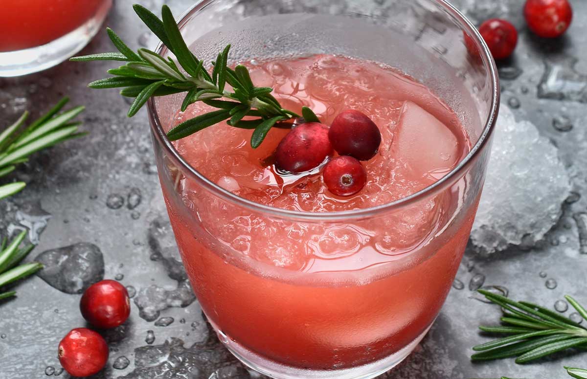 Glass of cranberry 国产xxxx视频在线观看 with fresh cranberries and a rosemary sprig for garnish, bowl of fresh cranberries in the background.