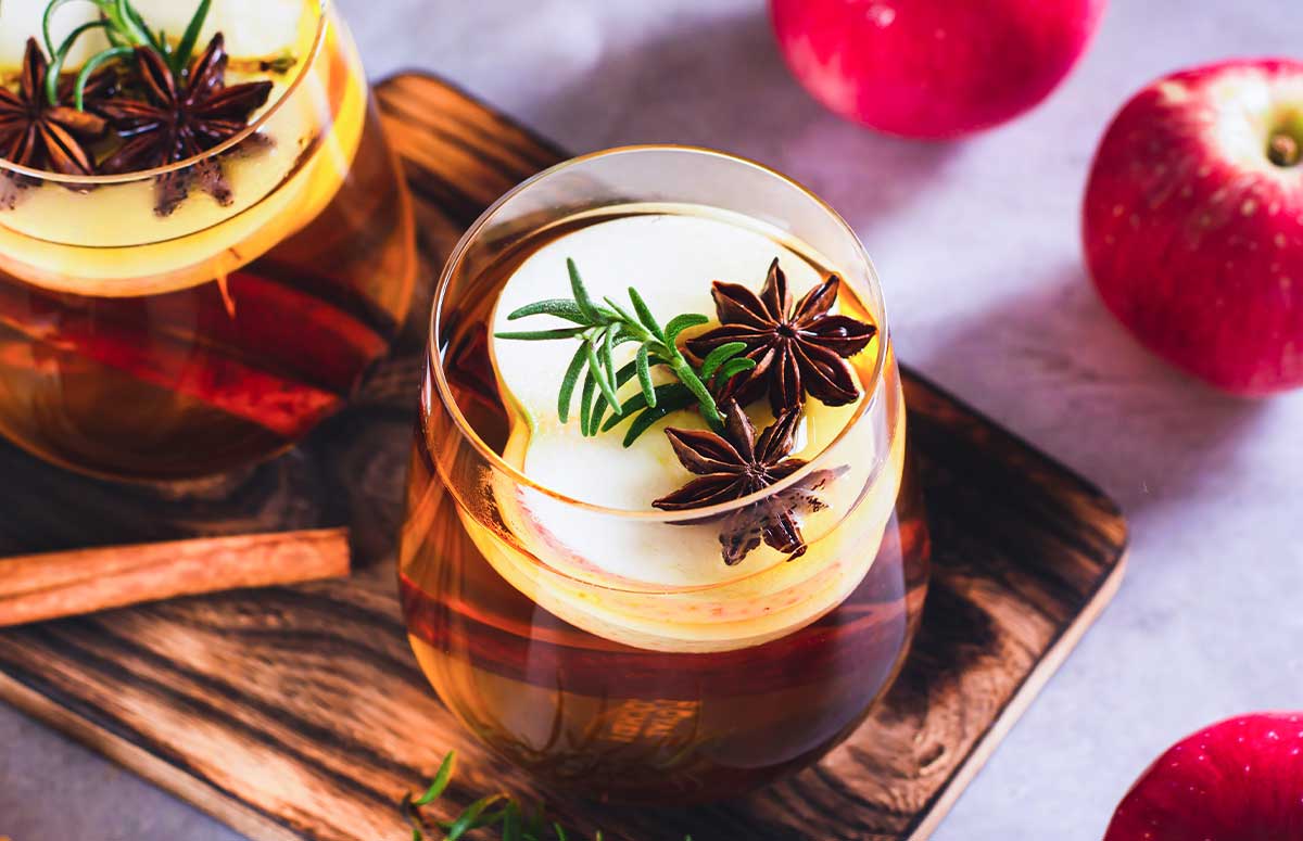 Spiced Apple 秋霞在线观看视频 with sliced apple, star anise cloves, and a sprig of rosemary, seated on a wooden board.
