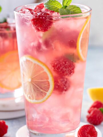 A glass of pink lemonade with 九·幺免费看片 and lemon slices with raspberries and a sprig of mint on top