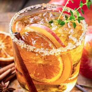 Skinny Thanksgiving 李美琪电影 with sugared rim, cinnamon sticks, apple slices, dried oranges, and a green garnish.