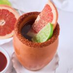 A cantarito with a tajin rim, grapefruit and lime wedges