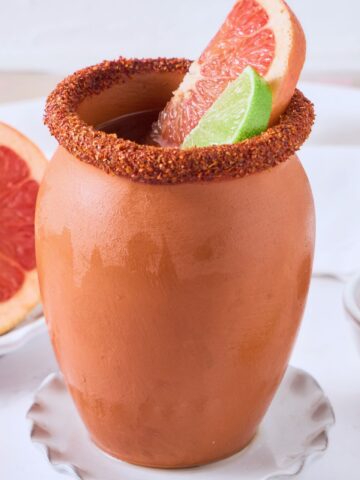 A cantarito with a tajin rim, grapefruit and lime wedges