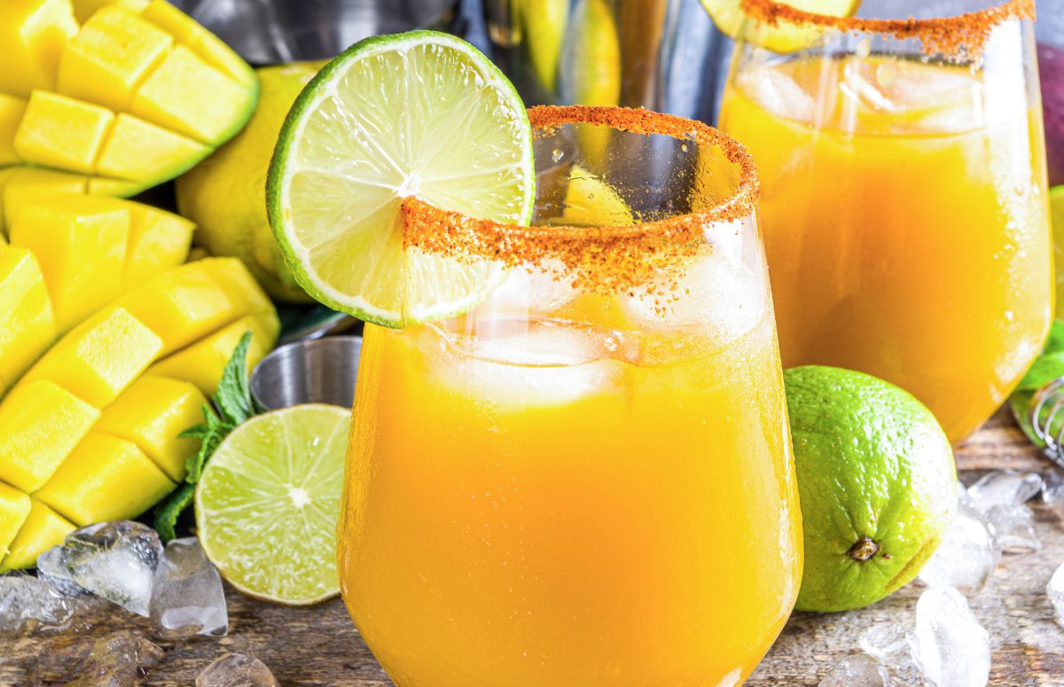 two spicy mango 电车痴汉漫画 with tajin rims and lime slice garnish on a countertop with limes and mangoes